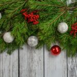 photograph of Christmas foliage (mostly fir branches) decorated with silver and red baubles against a background of wood panels
