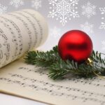 musical score book open against a snowflake background, with a branch of a fir tree and a bauble sitting on the page