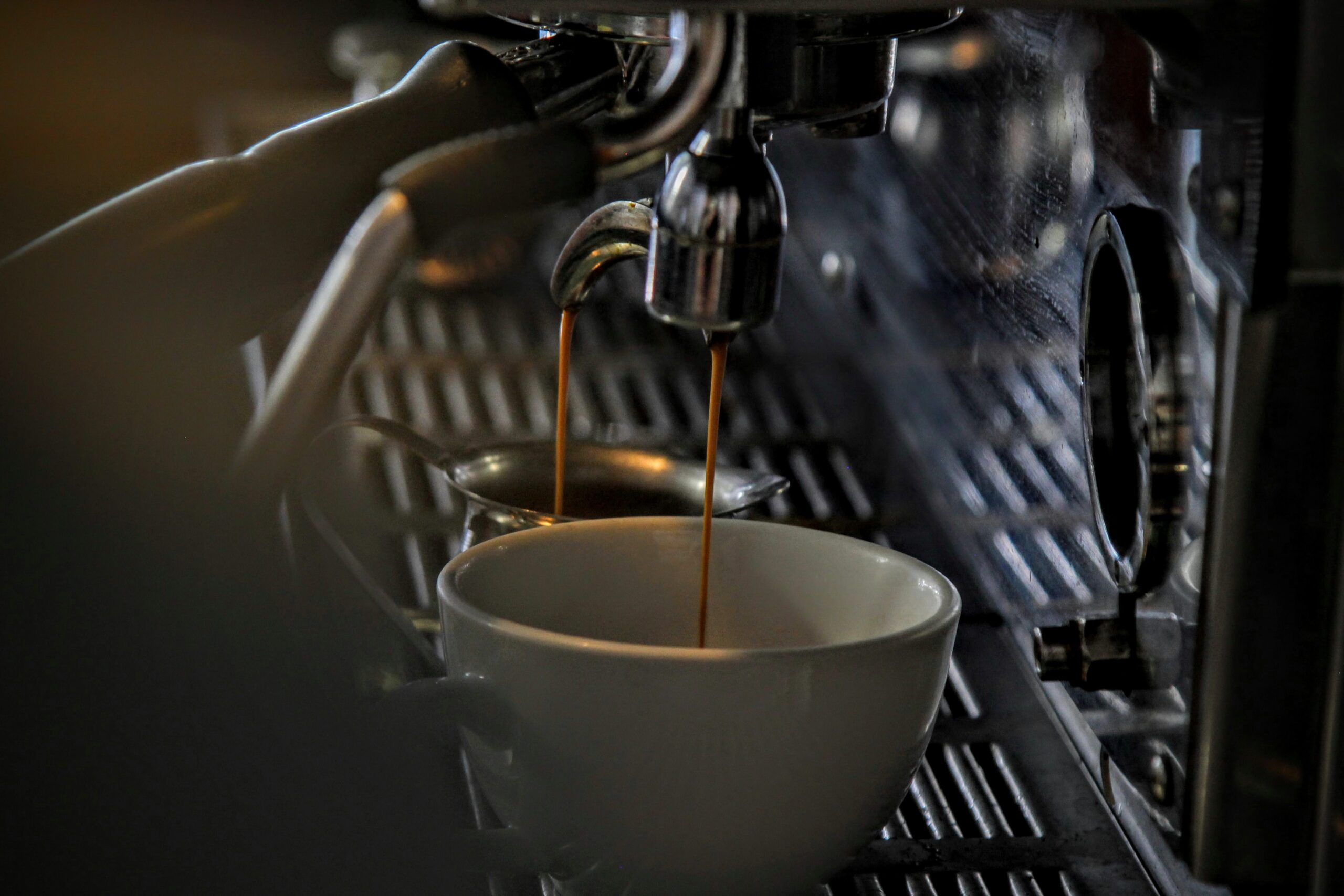 A white coffee cup underneath the spout of a barista machine, with coffee pouring in.